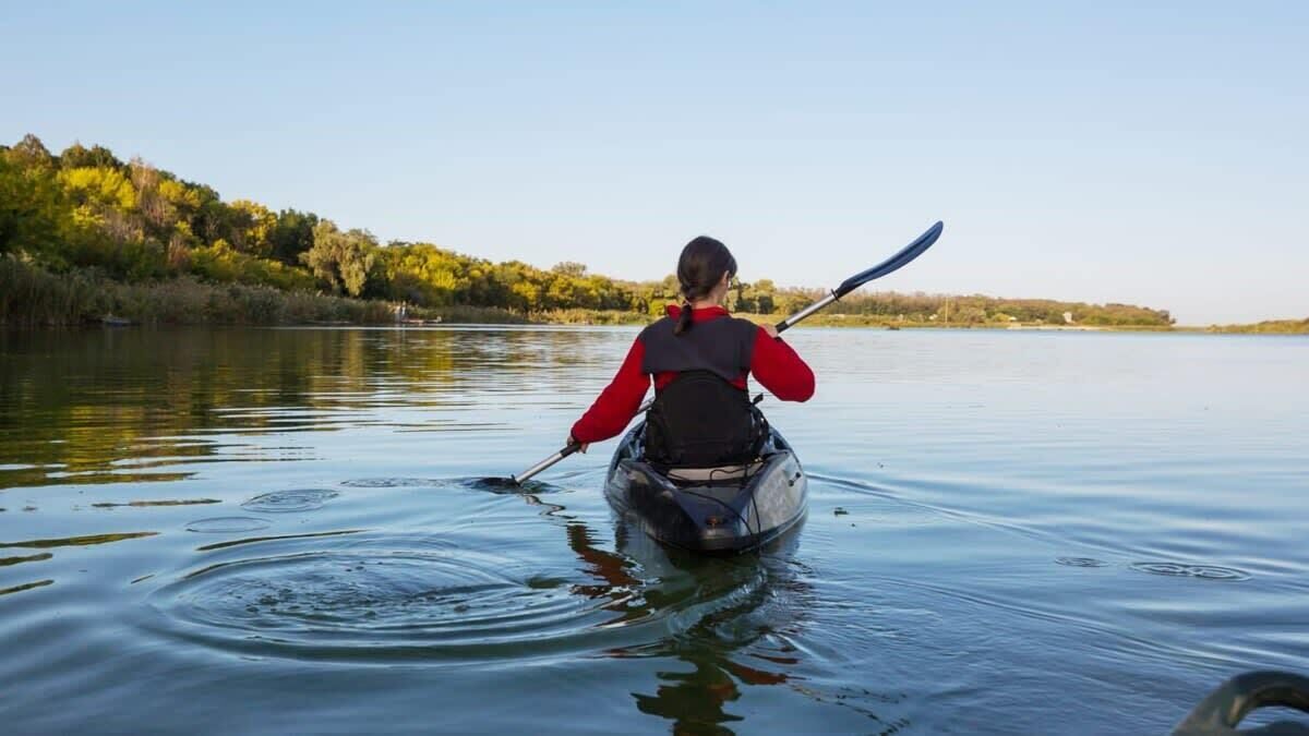 Une personne pratiquant le kayak sur un lac calme, avec des arbres en arrière-plan.