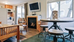 Ein gemütliches Wohnzimmer mit Kamin, Holzmöbeln, einem Fernseher und Blick ins Freie.