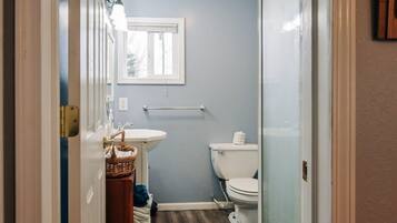 Une petite salle de bain avec un lavabo blanc, des toilettes et une fenêtre située au-dessus des toilettes.