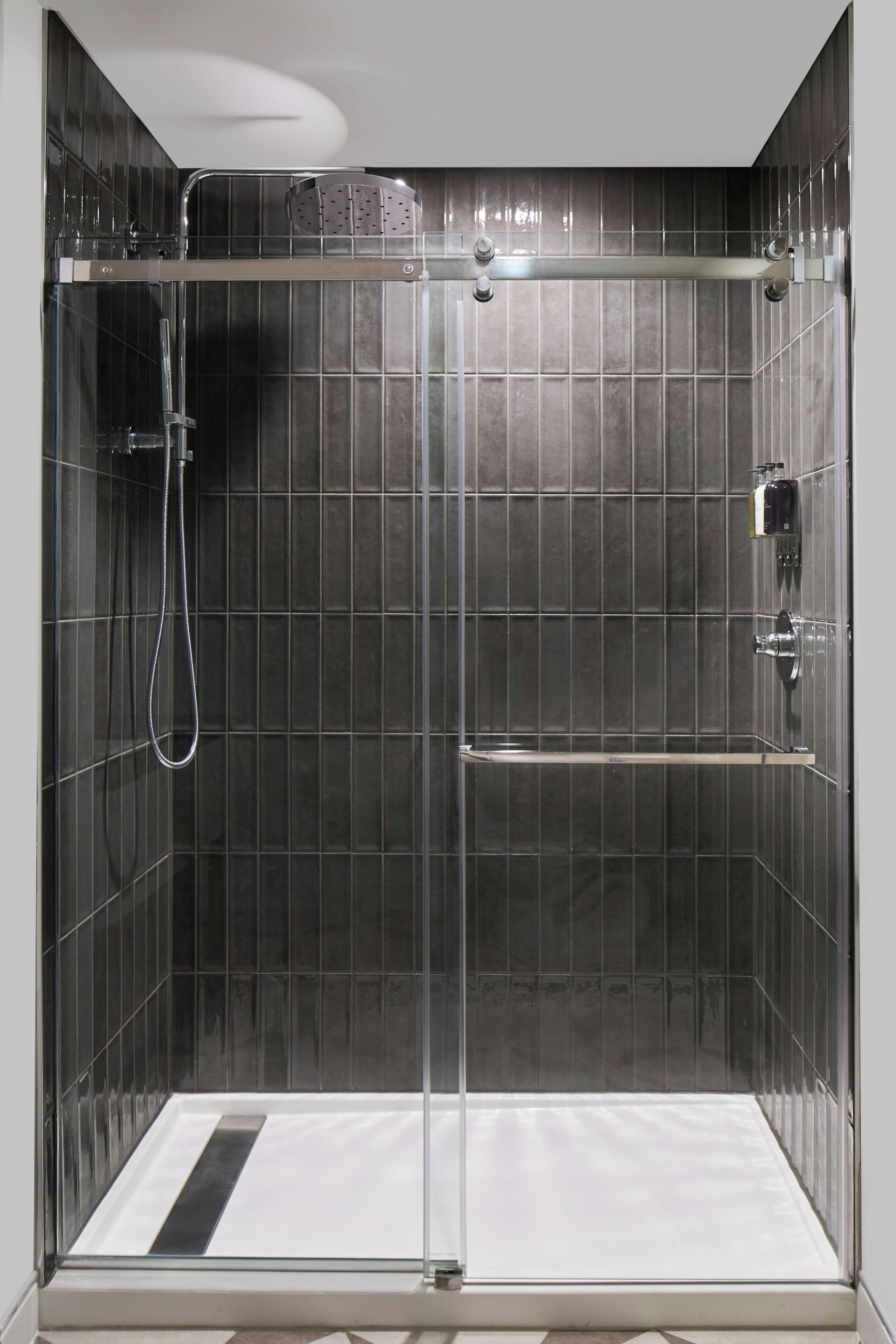 A modern shower enclosure with a glass door, a handheld showerhead, and a built-in shelf.