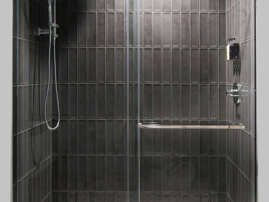 A modern shower enclosure with a glass door, a handheld showerhead, and a built-in shelf.