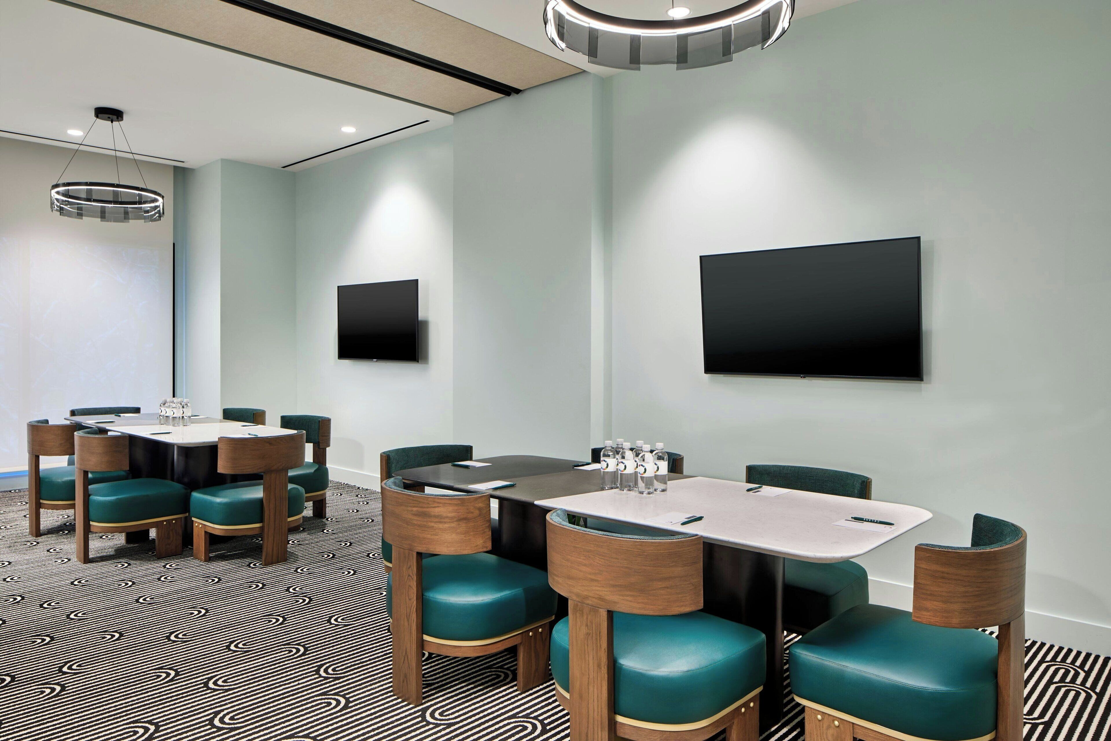 A conference room with a large table, chairs, a flat-screen TV, and a patterned carpet.