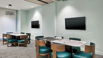 A conference room with a large table, chairs, a flat-screen TV, and a patterned carpet.
