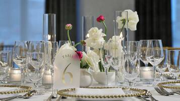 Mesa dispuesta para un evento formal, con sillas numeradas, cristalería transparente y flores decorativas.