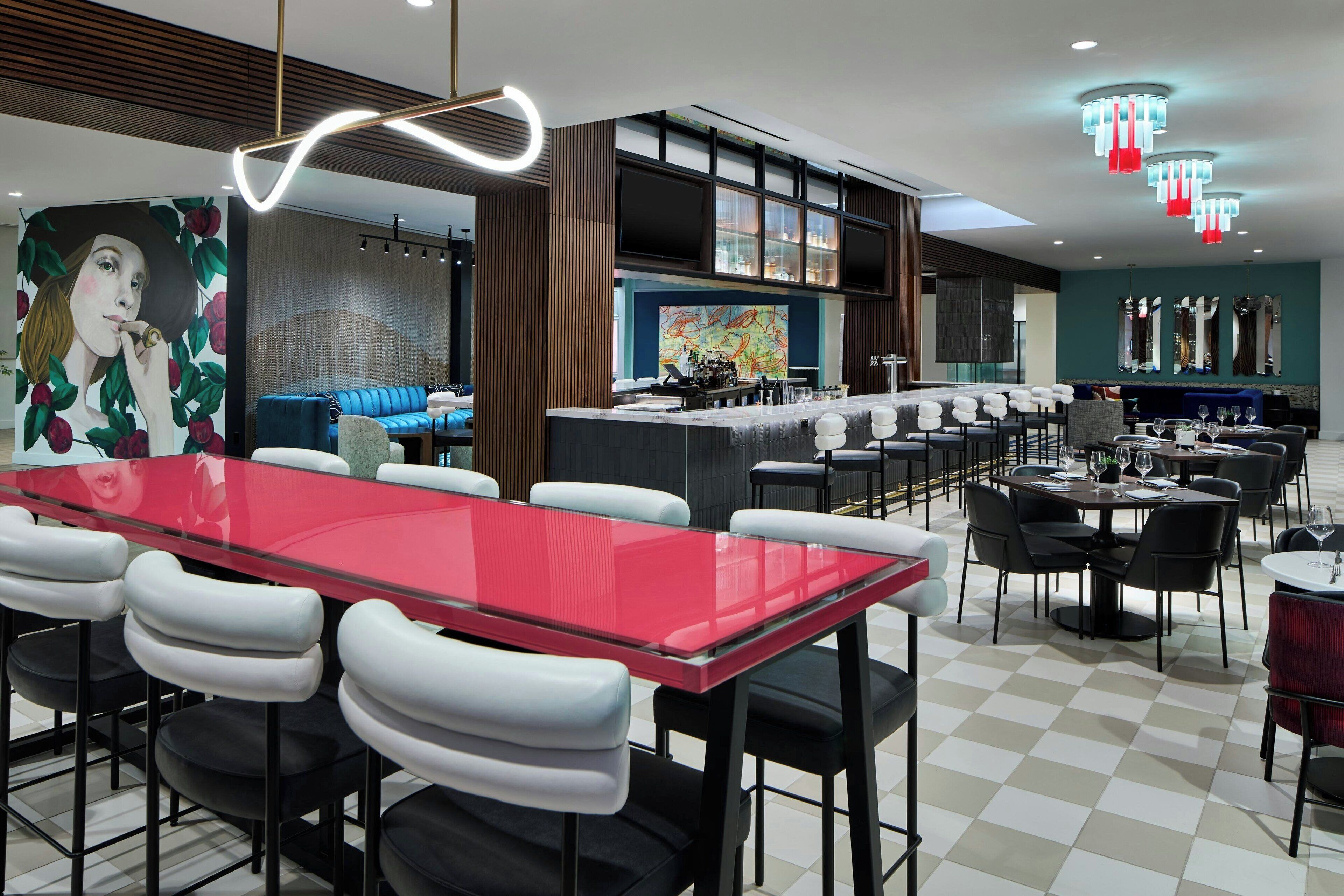 Un área de bar moderna con una mesa de vidrio roja, sillas blancas y negras, y un sofá azul.