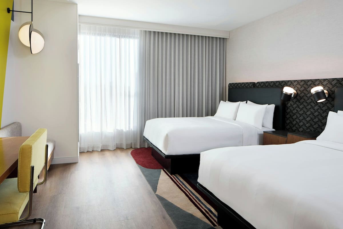 A hotel room with two beds, a desk, and a chair.