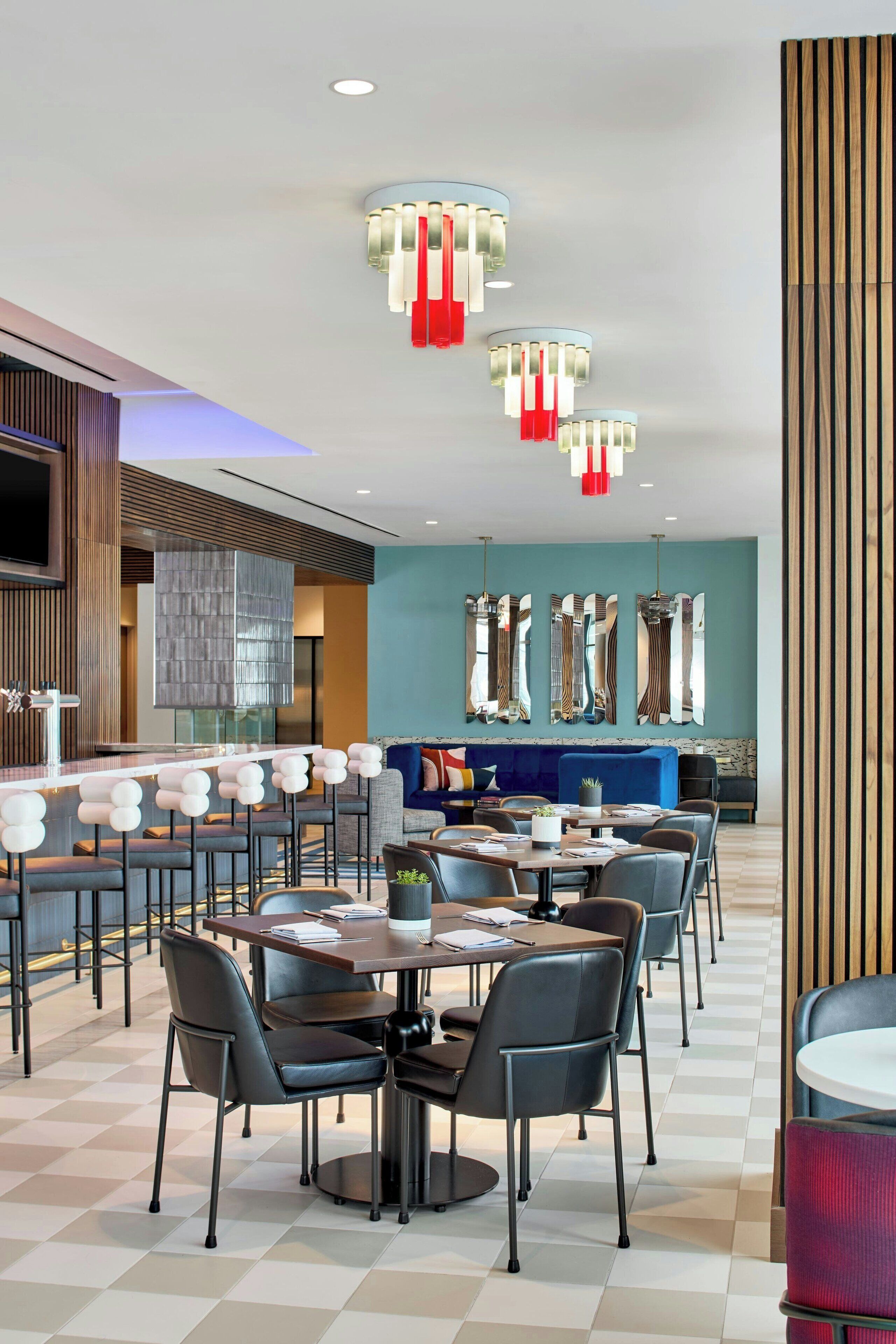 A modern dining area with multiple tables and chairs, a bar area with stools, and a seating area with a sofa and chairs.