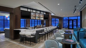 A modern bar area with a long counter, multiple stools, and a large TV screen. - Hotel Celare, Cincinnati Midtown, a Tribute Portfolio Hotel (Cincinnati)