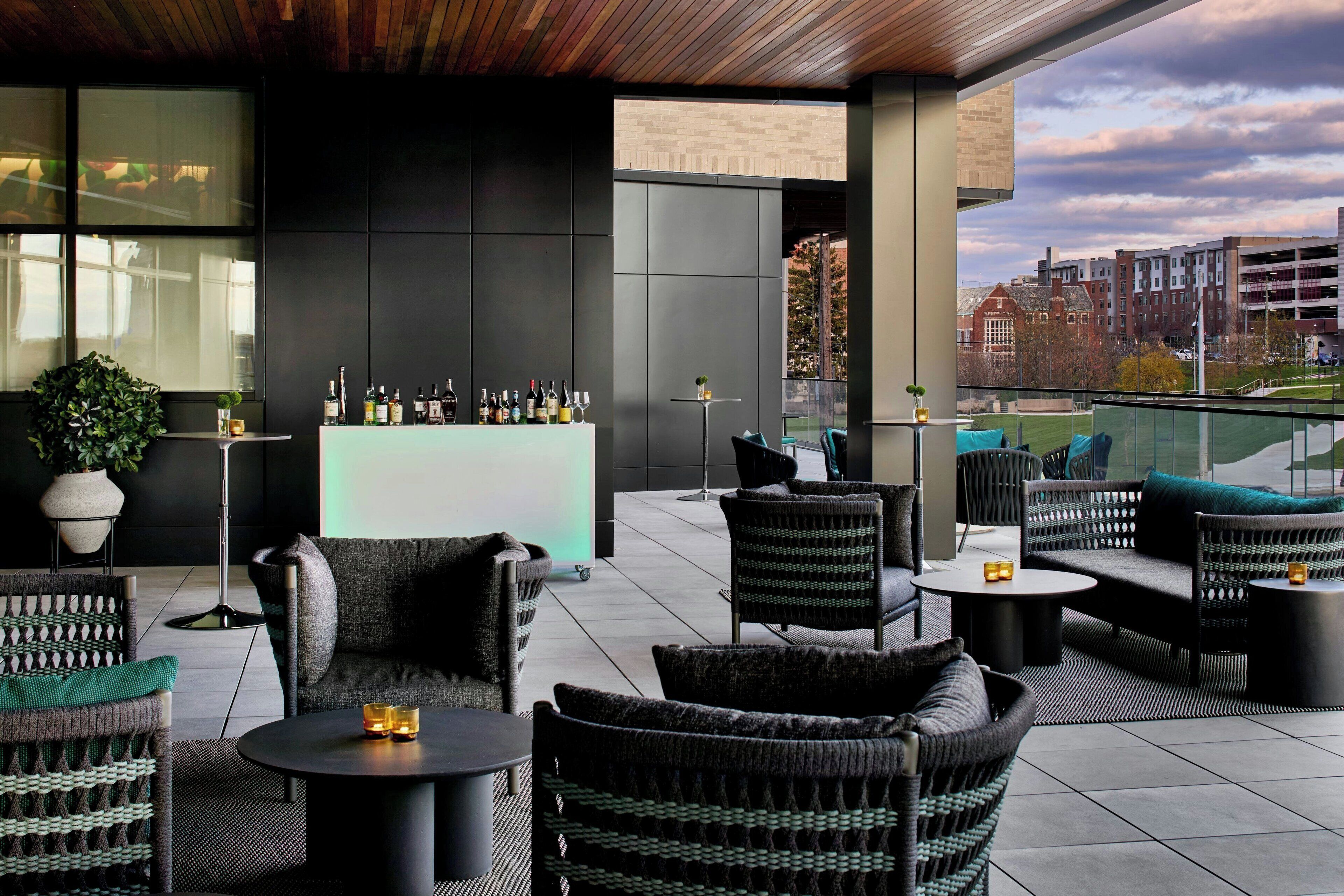 A modern outdoor seating area with wicker furniture, a bar with bottles, and a city view.
