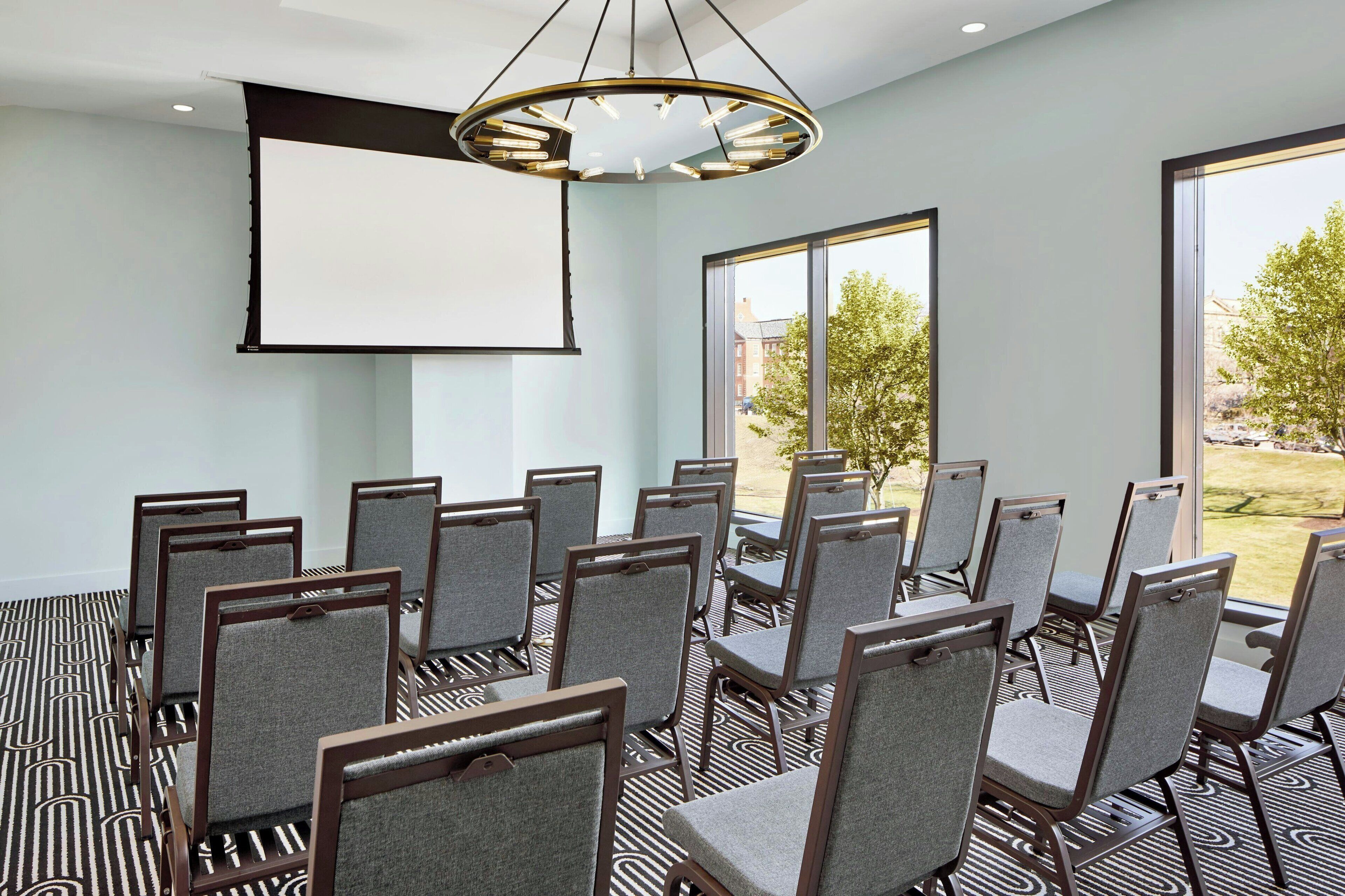 A conference room with a large screen, multiple chairs, and a patterned carpet.