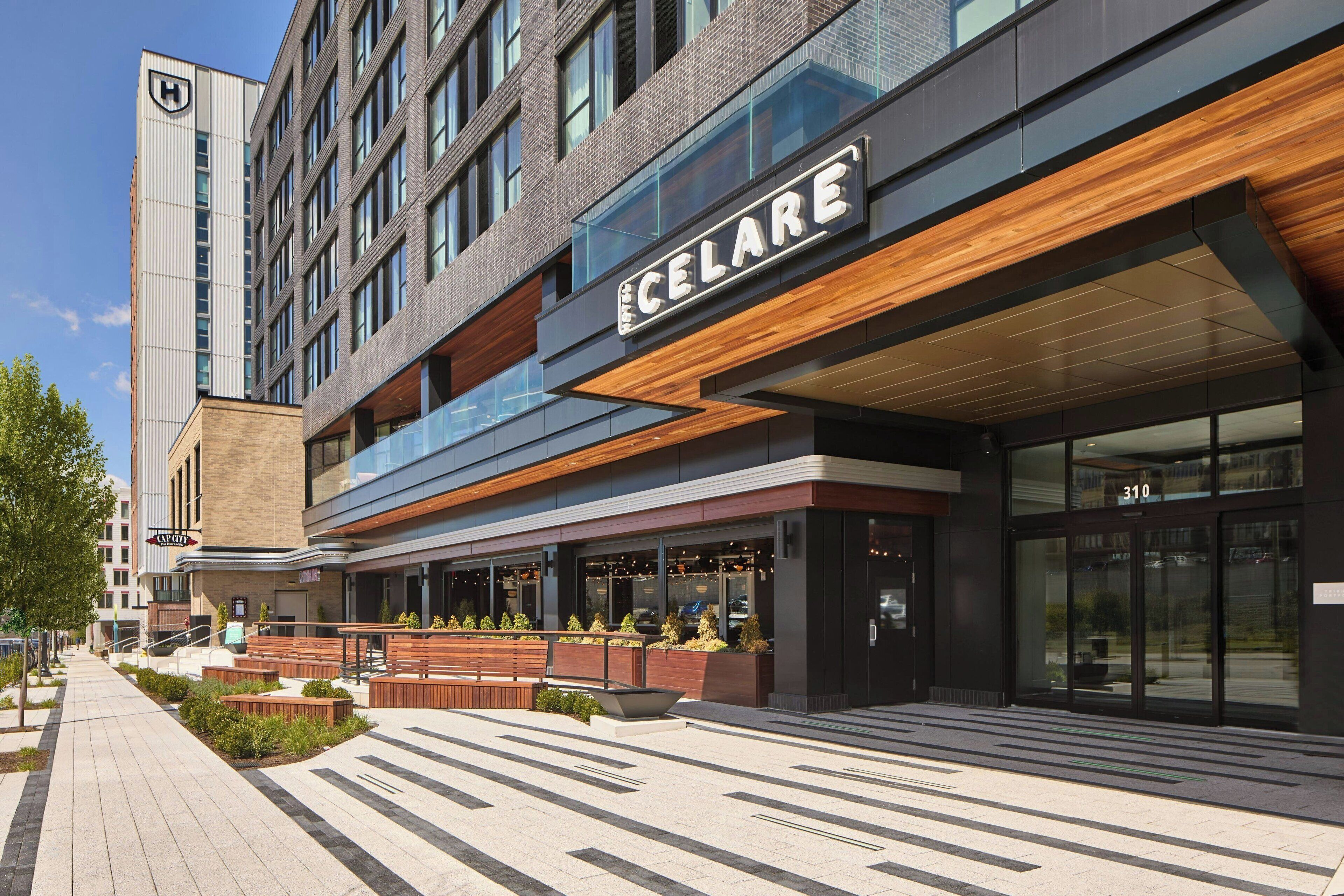 A modern hotel with a prominent 'CELARE' sign, outdoor seating, and a clear pedestrian pathway.