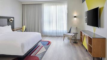 A hotel room with a bed, a desk, a chair, a TV, and a window with curtains.