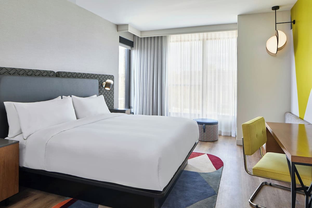 A hotel room with a large bed, a desk, a chair, and a window with curtains.