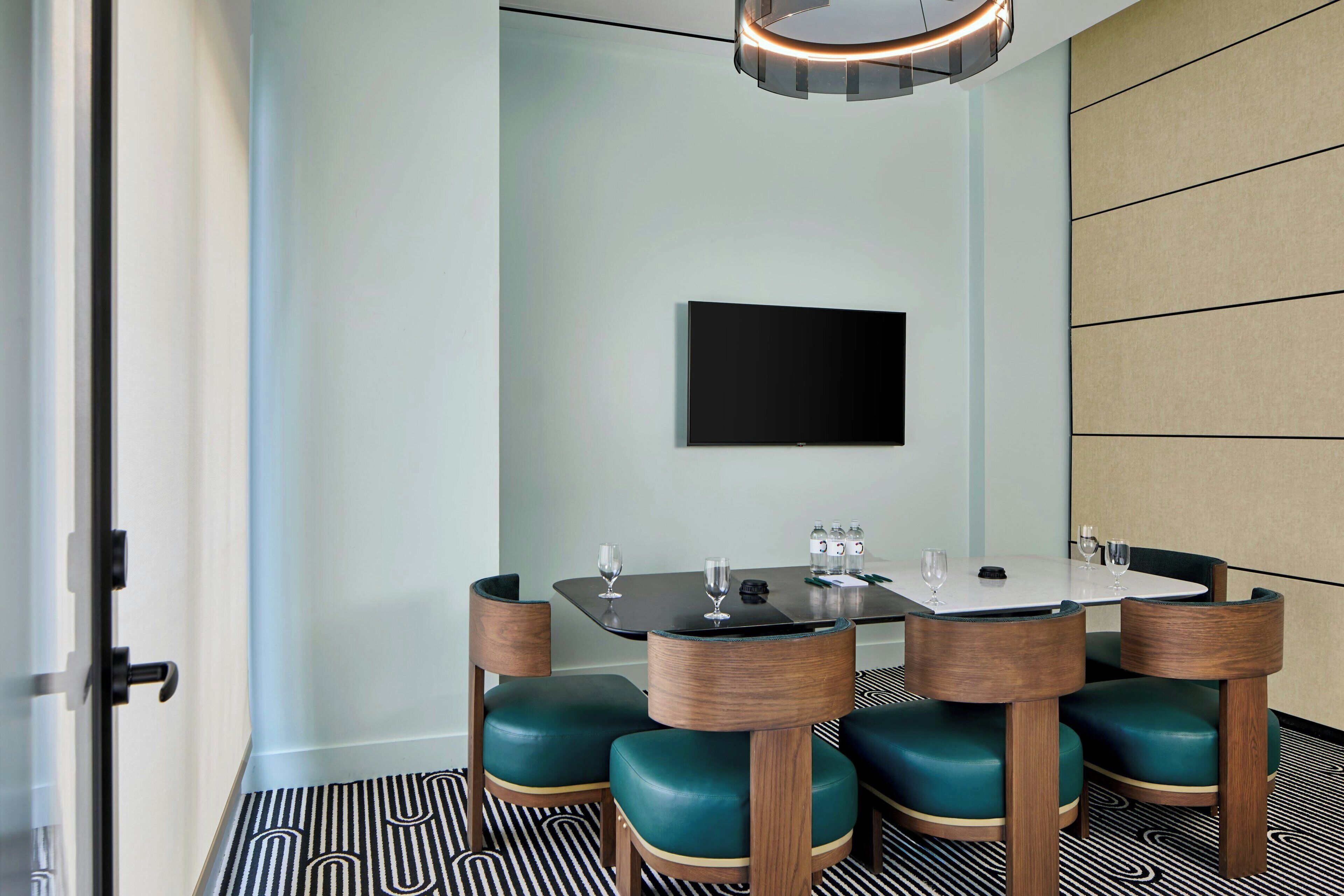 A conference room with a round table, four chairs, a flat-screen TV, and a patterned floor.