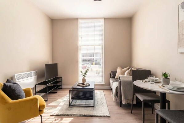 A modern living room with a sofa, a coffee table, a TV, and a dining area with a table and chairs.