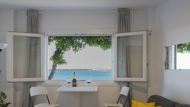 Una habitación con vista al mar, una mesa con dos sillas, un sofá y un jarrón con flores.
