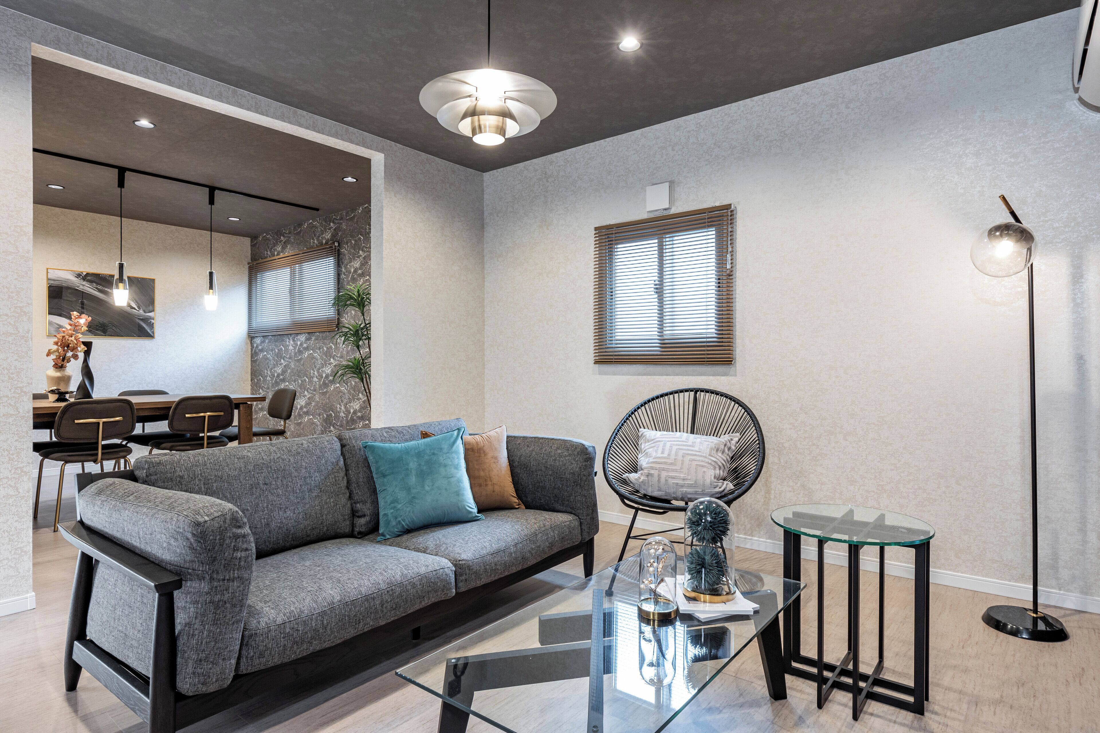A modern living room with a grey sofa, a glass coffee table, and a dining area with a wooden table and chairs.