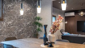 A modern dining area with a marble wall, a wooden dining table, blue chairs, and a vase with flowers. - JAPAVISTA Dusk (Osaka)