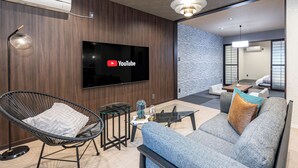 A modern living room with a flat-screen TV, a comfortable sofa, a wicker chair, and a glass coffee table. - JAPAVISTA Dusk (Osaka)
