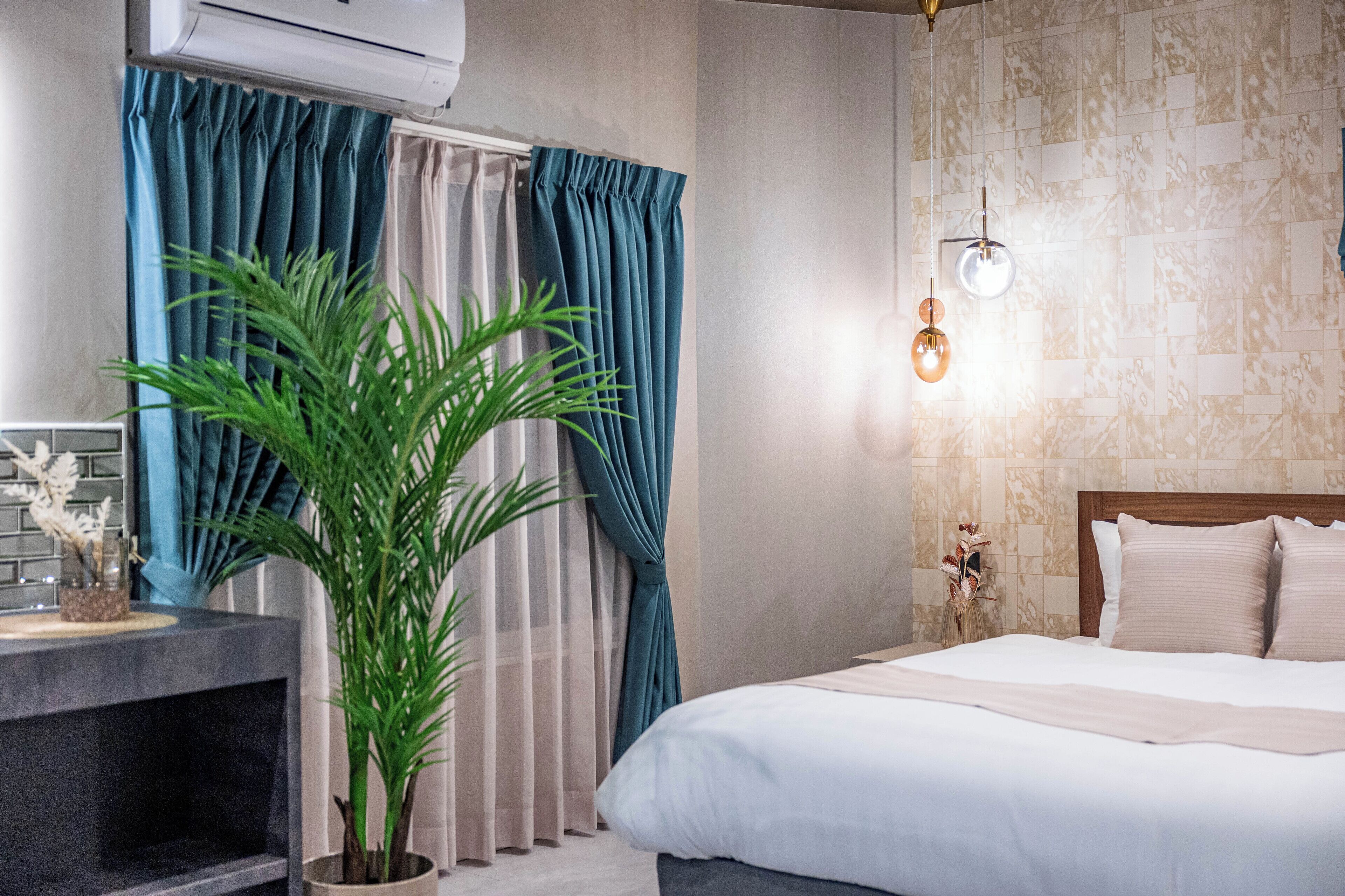 A bedroom with a bed, a potted plant, a nightstand with a vase, and a wall-mounted light fixture.