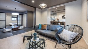 A modern living room with a sofa, a glass coffee table, a black chair, and a hanging light fixture. - JAPAVISTA Dusk (Osaka)