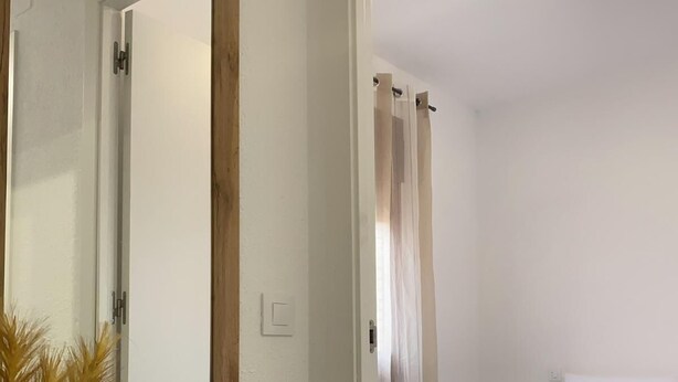 Un dormitorio con cama, espejo y lámpara de techo.