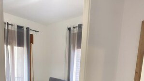 Una sala de estar con un sofá gris, una mesita de madera con un cuenco, un tapete colorido y una alta jarra blanca con plantas secas.