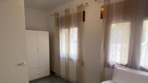 Un dormitorio con cama, armario y ventana con cortinas translúcidas.