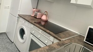 Cocina compacta con armarios blancos, lavadora, estufa y pileta.