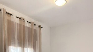 Una habitación de hotel con cama, mesita de noche y cortinas traslúcidas.
