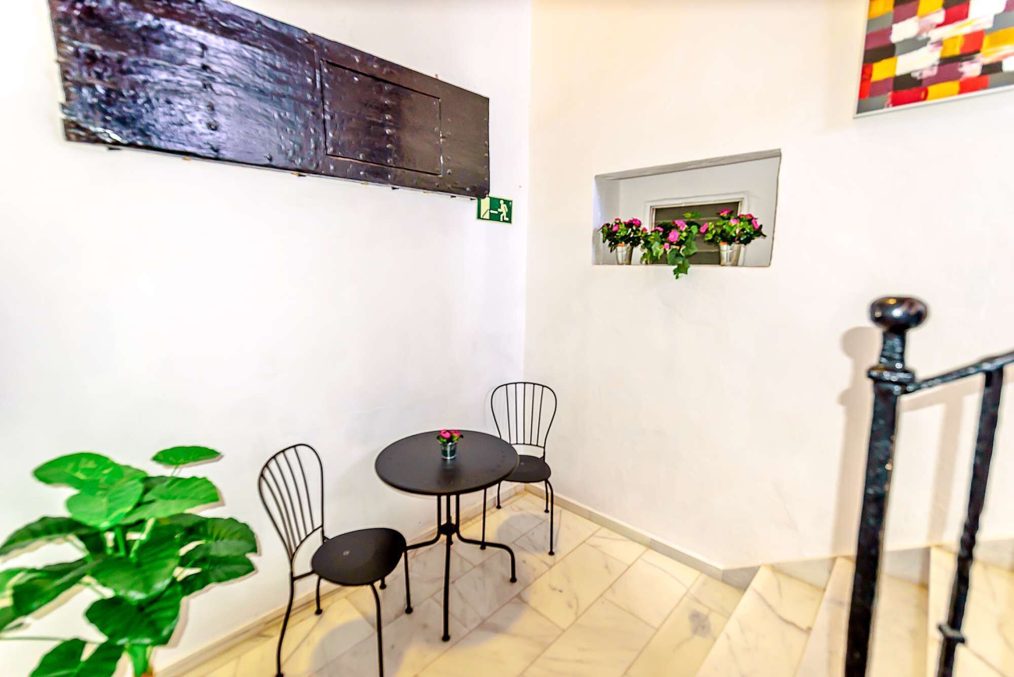 Ein kleiner Essbereich mit Tisch und Stühlen, einer Topfpflanze und einem an der Wand befestigten Regal mit Blumen.