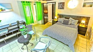 Ein Schlafzimmer mit Bett, Nachttischen, einem Sessel, einem kleinen Tisch mit Pflanze und Vorhängen.