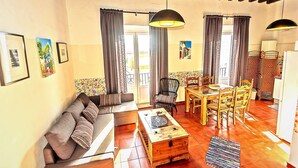 A cozy living room with a sofa, coffee table, and dining area with chairs. There are curtains, a painting, and a wooden ceiling. - Milagros #3, three-bedroom Central Apartment (El Puerto de Santa María)