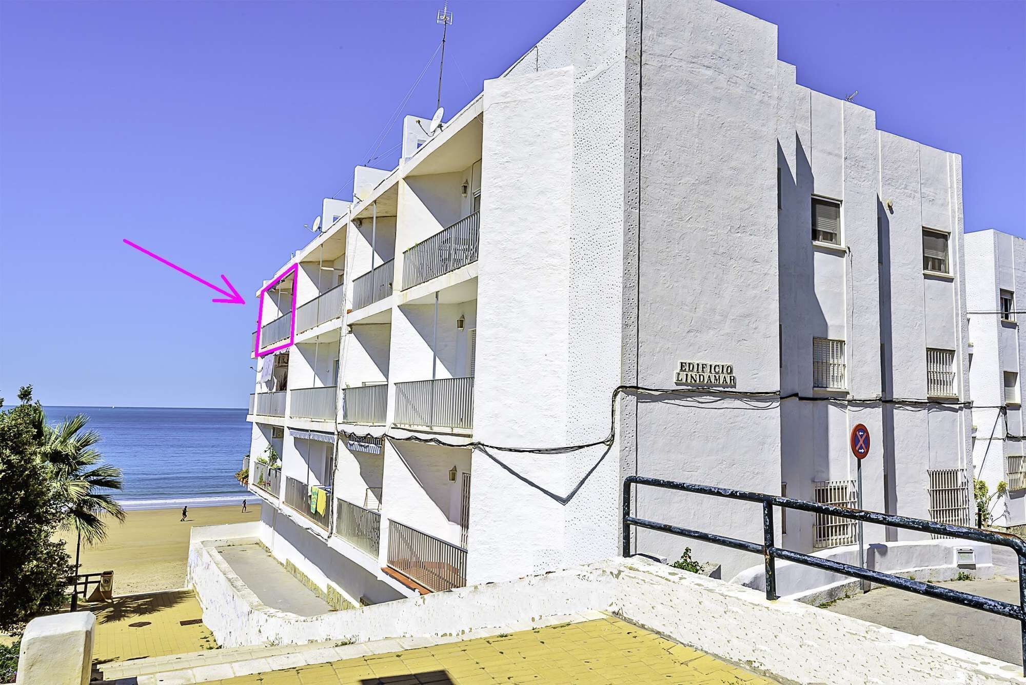 Un edificio de varios pisos con balcones y vista a la playa, con un letrero que dice 'EDIFICIO LINDAMAR'.