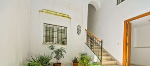 Amplio espacio interior con una escalera, plantas en macetas y una ventana con rejas.