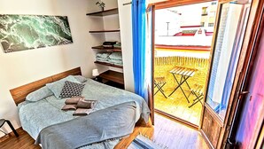 A bedroom with a bed, a shelf with folded blankets, a wall-mounted air conditioner, and a view of a wooden deck through a glass door.