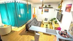 A modern living room with a sofa, a coffee table, and a TV. There are plants, a curtain, and a ceiling light.