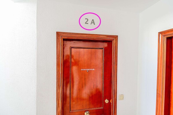 Una puerta de madera con una etiqueta que dice "APARTAMENTO" y el número "2A" encerrado en un círculo.