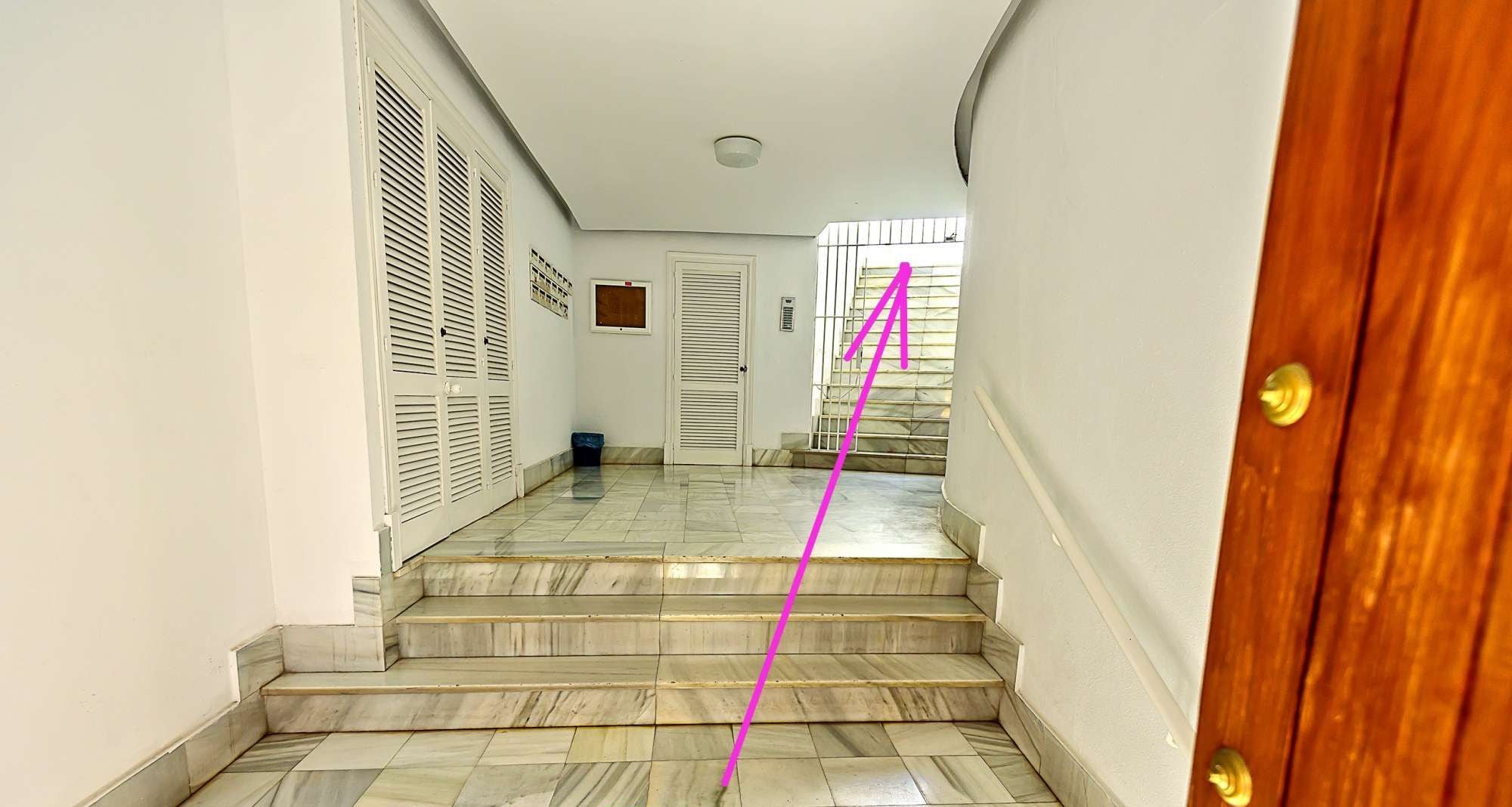 A hallway with marble flooring leading to a wooden door.
