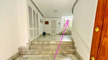A hallway with marble flooring leading to a wooden door.