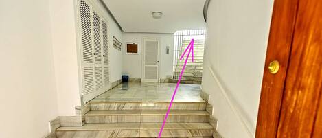 A hallway with marble flooring leading to a wooden door.