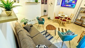Una sala moderna con un sofá, sillas, una mesita y un televisor mostrando la interfaz de un servicio de streaming.