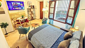 Habitación de hotel con cama, escritorio, silla, televisor y ventana con cortinas.