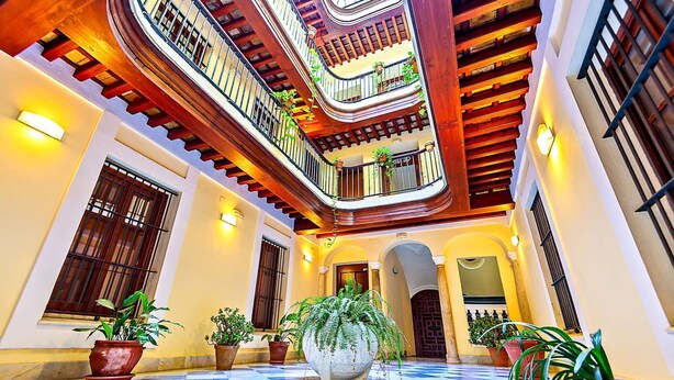 Un atrio de varios niveles con suelo a cuadros, balcones de madera y plantas en macetas.