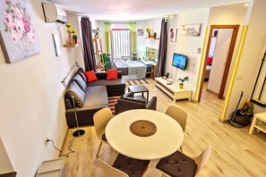 A modern living room with a sofa, a dining table with chairs, a TV, and a small kitchen area. - Plaza Herrería Central Apartment "E" with Balcony. Right downtown, best location (El Puerto de Santa María)