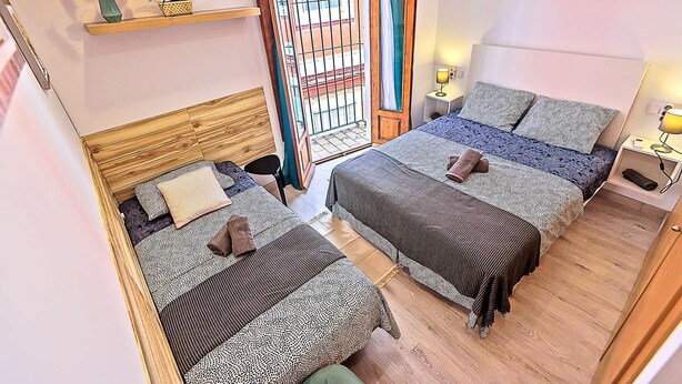 A hotel room with two beds, a wooden headboard, a large window with a view, and a shelf with decorative items. - Plaza Herrería Central Apartment "D" with Terrace. Right downtown, best location (El Puerto de Santa María)