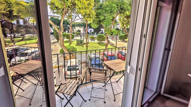 A balcony with a view of a park, a car, and a building in the background. - Plaza Polvorista 4-Bedroom Apartment with Balcony in front of the beautiful park (El Puerto de Santa María)