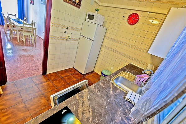 A kitchen with a marble countertop, a sink, a refrigerator, and a microwave.