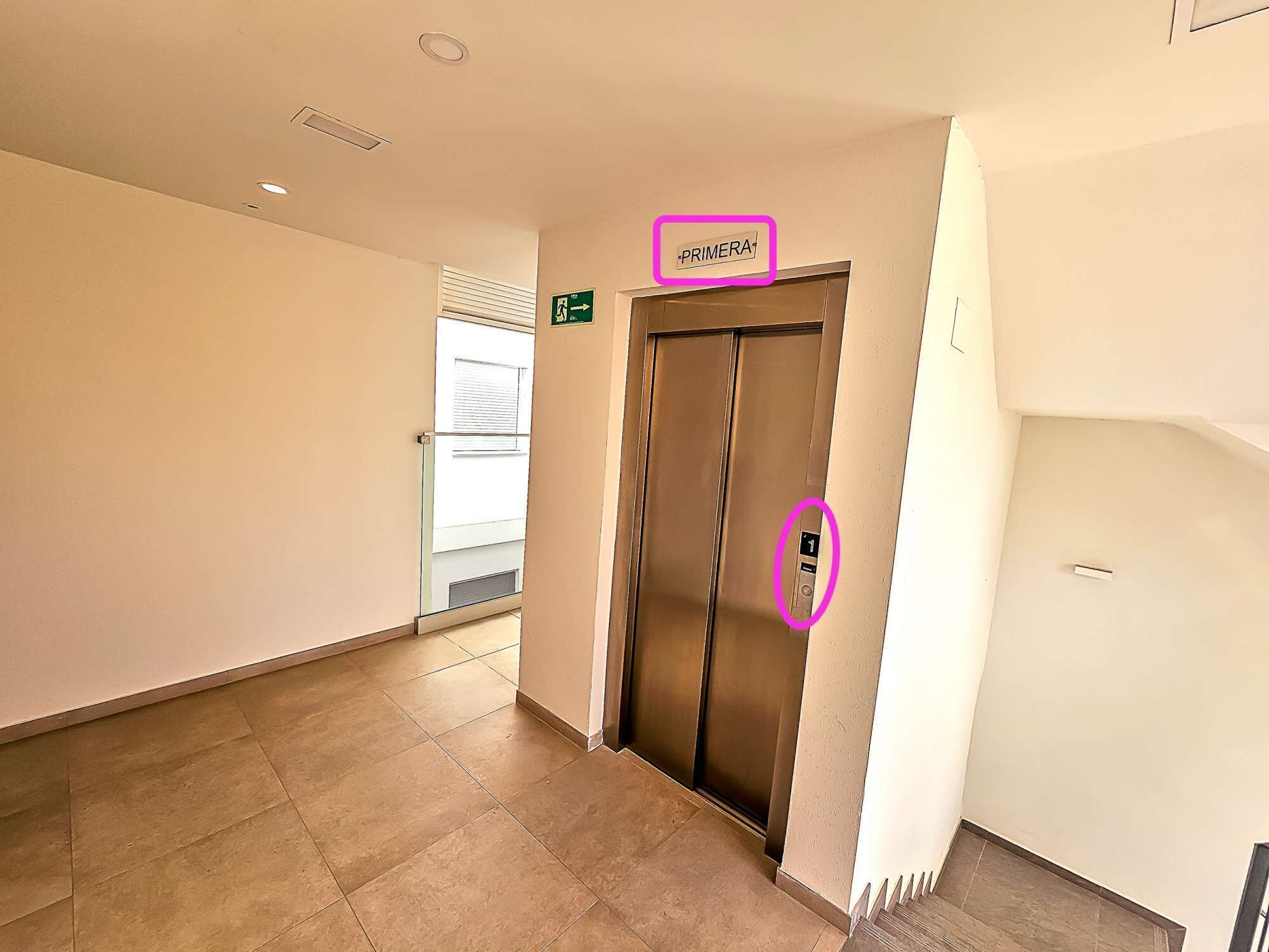 Ein Flur mit Aufzug, einer Tür mit Schild für die erste Etage und einem Brandschutztürschild.