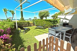 Eine Terrasse mit Tisch und Stühlen, einem Grill und Blick auf den Strand.